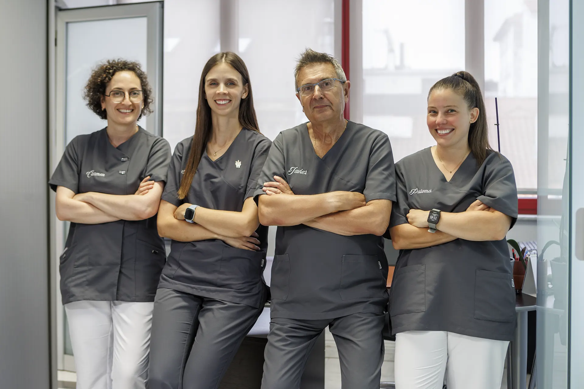 Tras mujeres y un hombre con los brazos cruzados y sonriendo, posando apoyados en una mesa