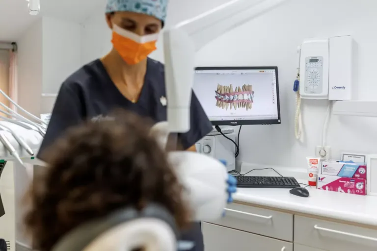 Andrea mientras atiende a una paciente y en la parte de atrás una pantalla con una recreación 3d de una dentadura